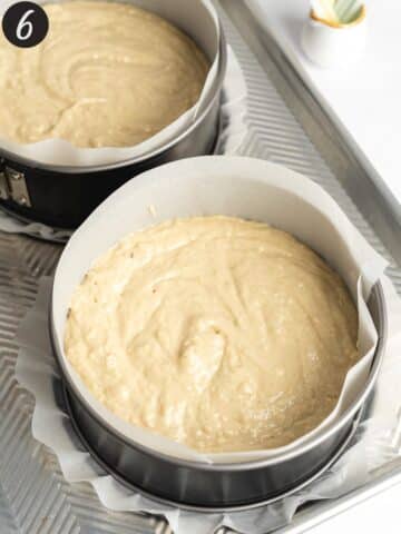 vanilla cake batter distributed between 2 cake pans on a aluminium tray before baking.
