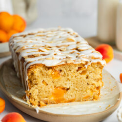 apricot cake topped with flaked almonds and sugar glaze on a ceramic plate.