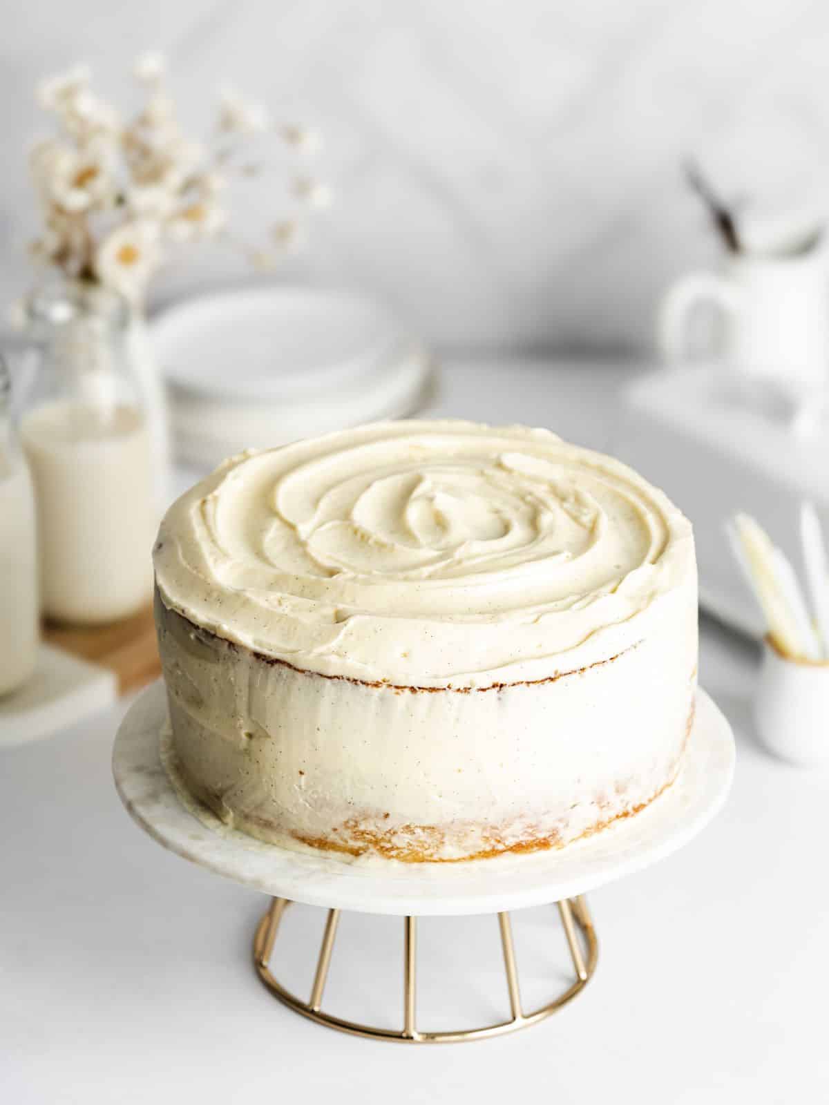 a vanilla cake with swirled vanilla frosting on a marble cake stand with a white background.