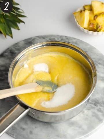 pineapple puree and sugar in a saucepan with a rubber spatula stirring it.