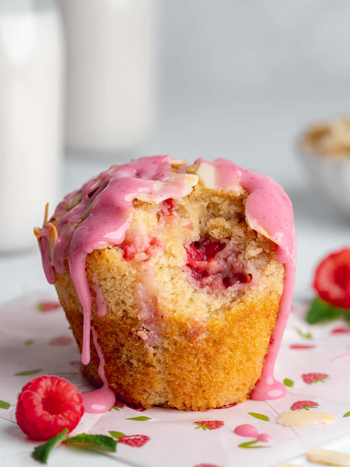 a raspberry muffin with a bite taken out of it and pink raspberry glaze flowing over the edges.
