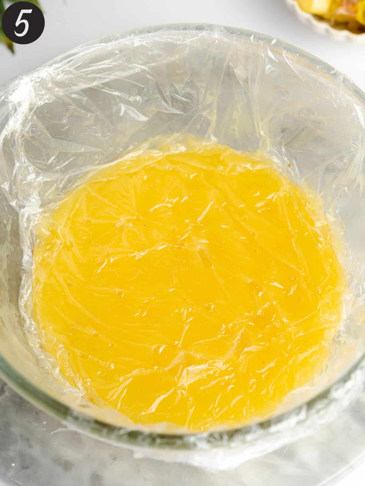 pineapple curd in a bowl covered in plastic wrap.