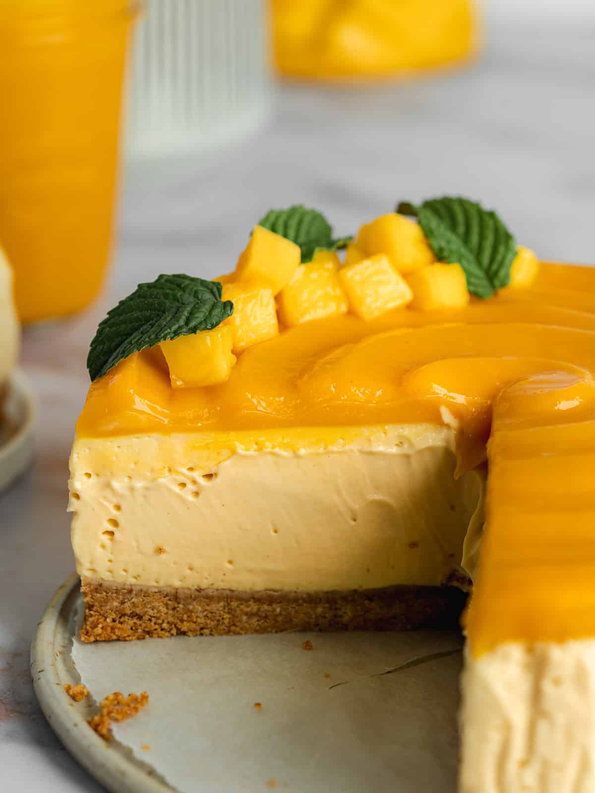 mango cheesecake with curd topping and fresh mango chunks on top with a few slices missing, showing the cross-section of creamy filling.