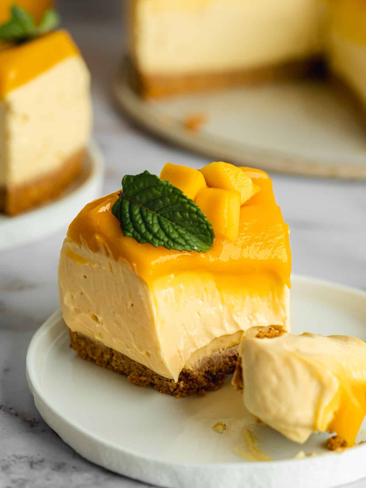 a slice of mango cheesecake with curd topping and a spoonful taken from it, showing the rich and creamy consistency.