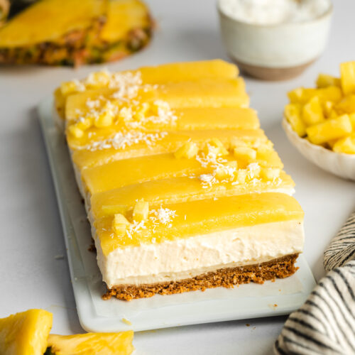 pineapple coconut cheesecake bars on a rectangular white plate with pineapple chunks and shredded coconut on top.