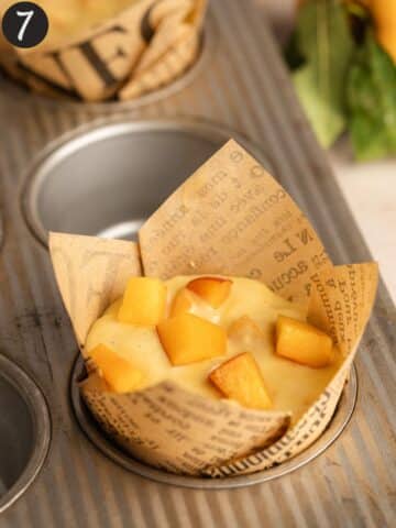 peach muffins in paper tulip liners with fresh peach chunks on top.