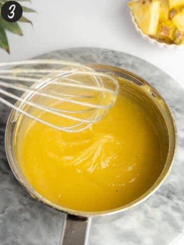 thickened pineapple curd in a saucepan with a whisk.