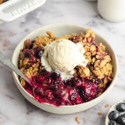 a bowl of vegan berry crumble with a scoop of vanilla ice cream on top.