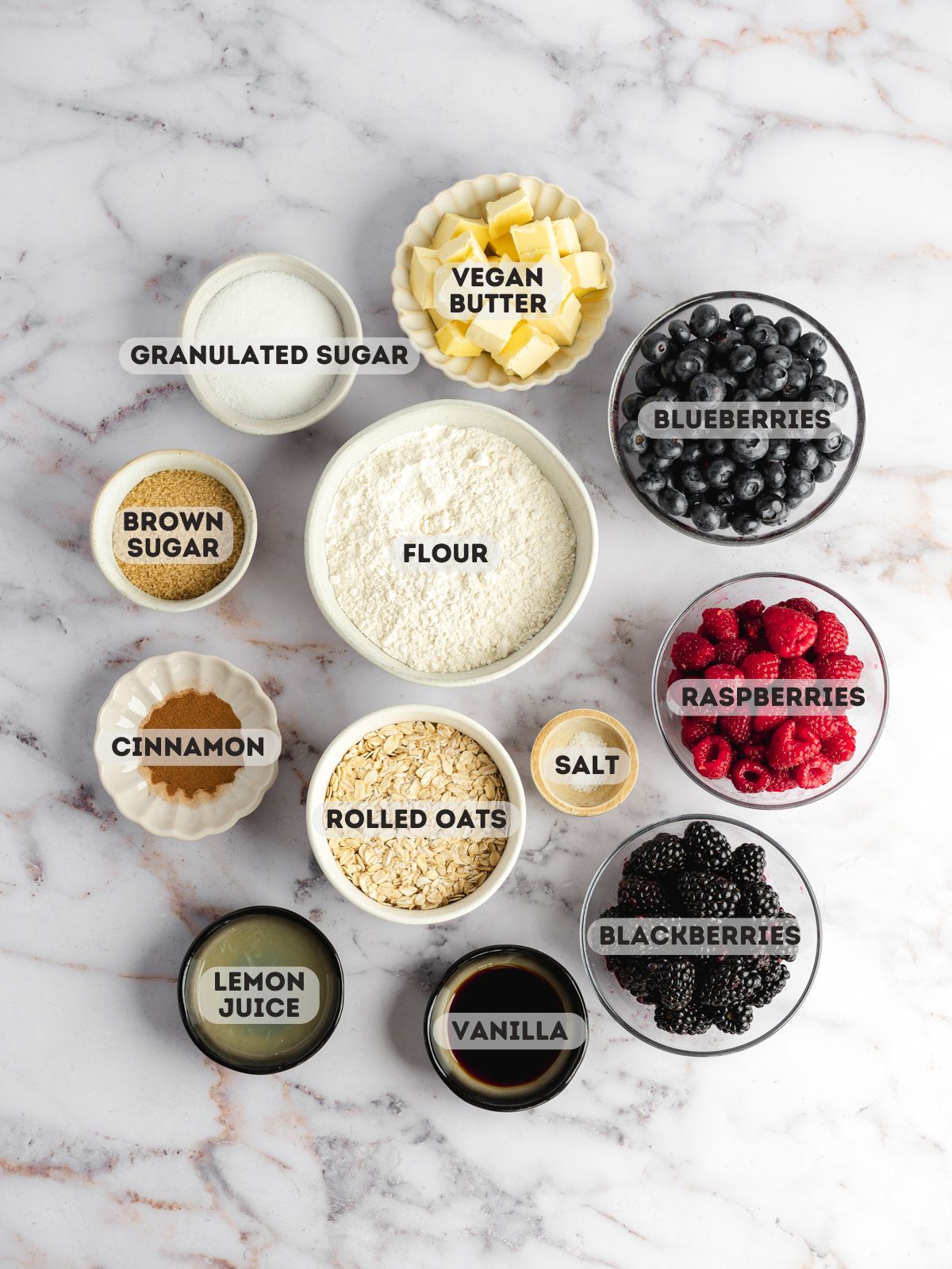 ingredients to make vegan berry crisp measured out in bowls on a marble surface.