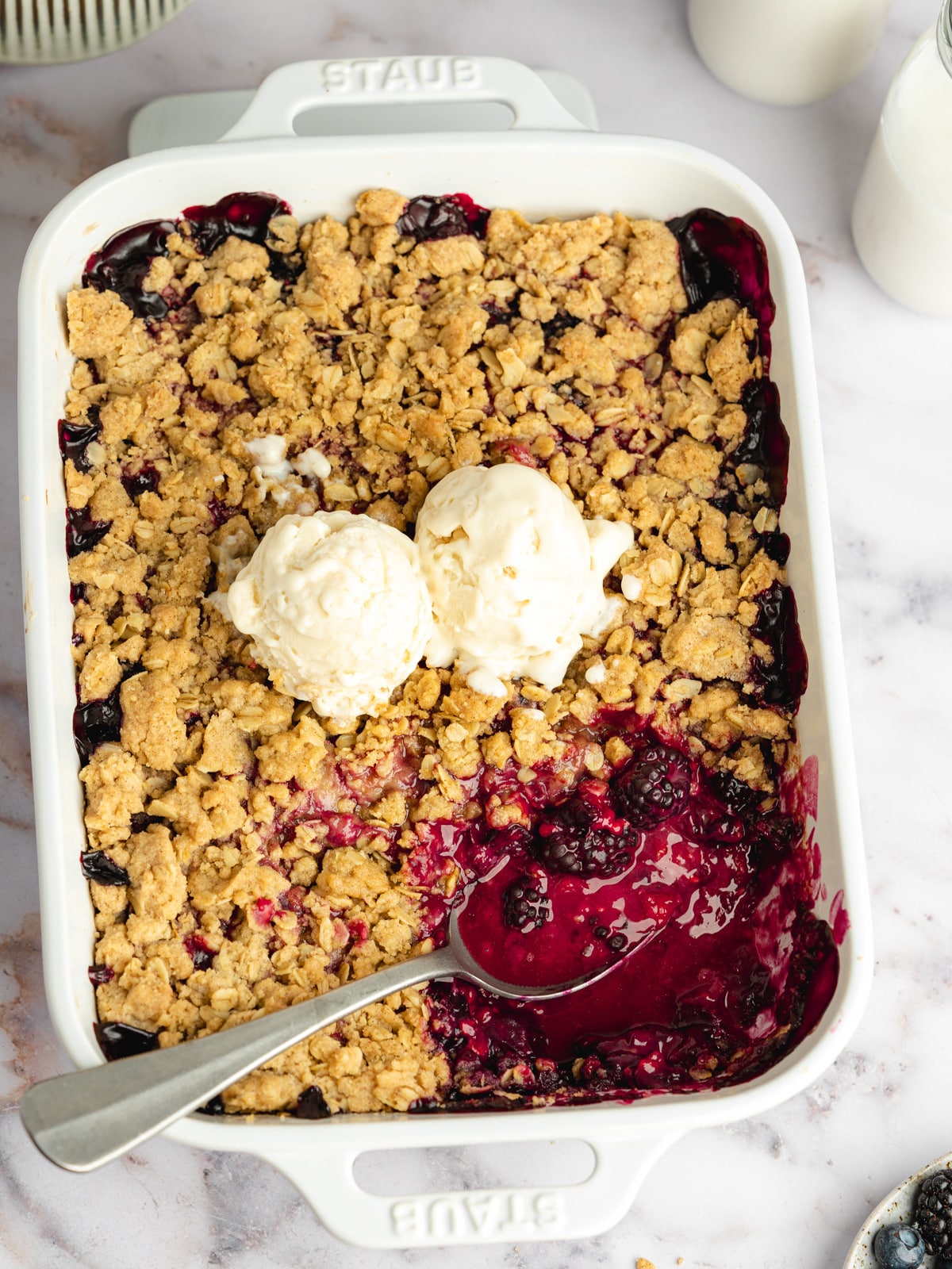 a baked blueberry vegan crisp with a spoon in it and 2 scoops of ice cream on top.
