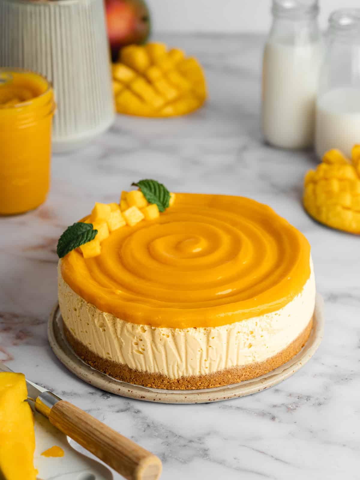 a mango cheesecake decorated with mango curd and fresh mango chunks on a marble surface.