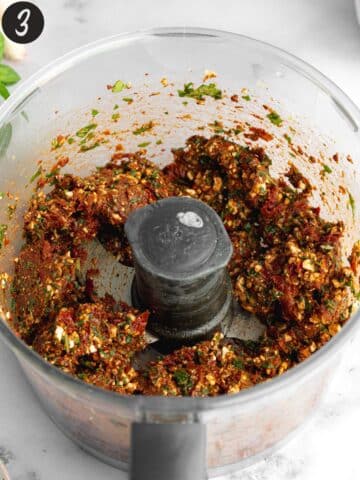 red pesto ingredients in a food processor jug which have been blended to a chunky paste.