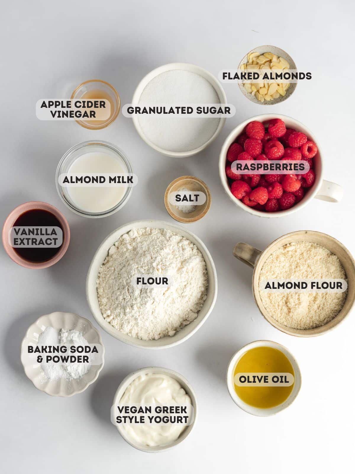 ingredients to make vegan raspberry muffins measured out in ceramic bowls on a gray surface.