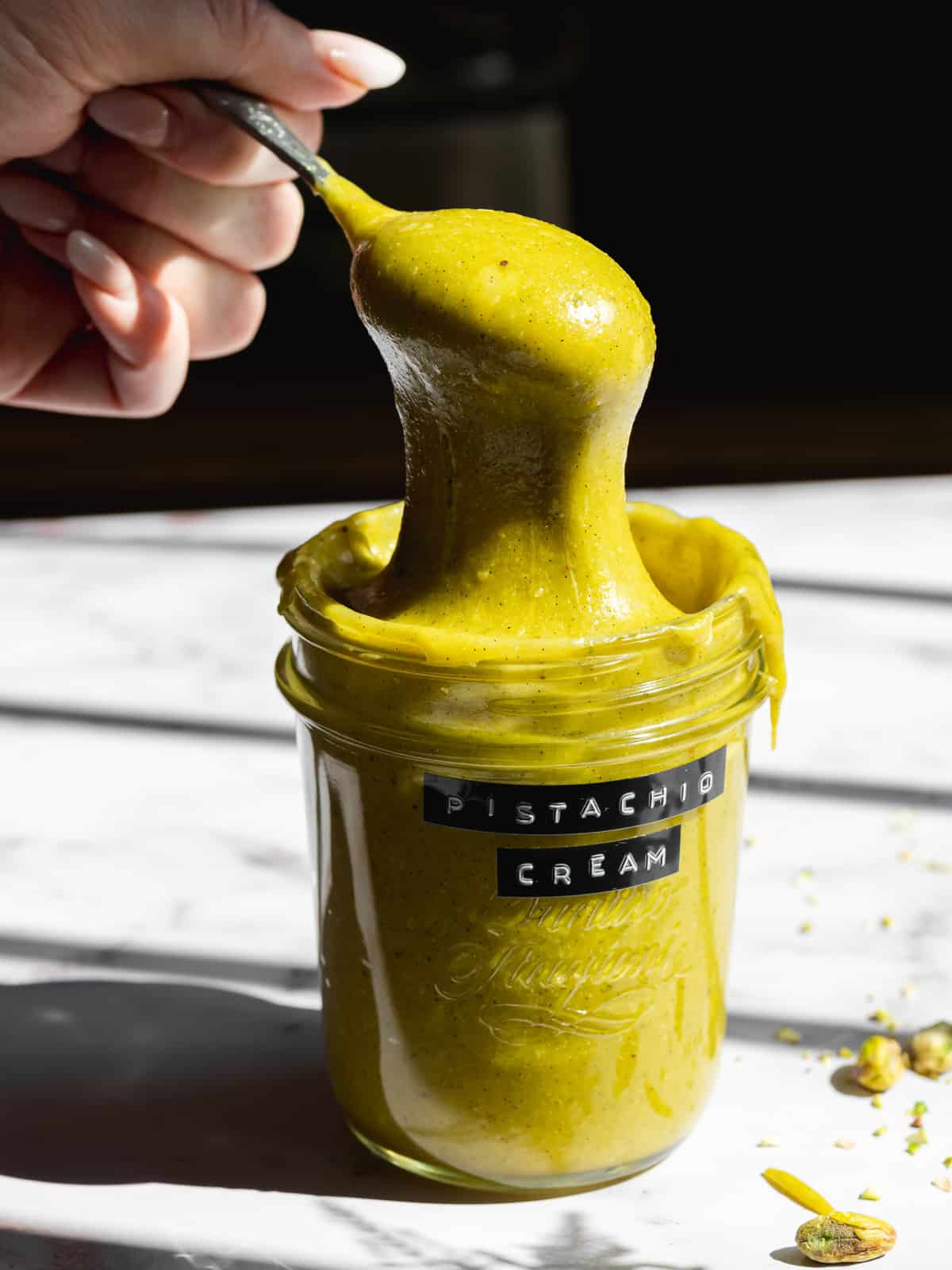a mason jar labeled as pistachio cream with a spoonful being lifted out showing the thick consistency.