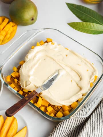 spreading the first layer of mango mascarpone over a mango tiramisu with an offset spatula.