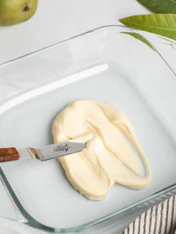 spreading mango mascarpone in the base of a glass dish with an offset spatula.