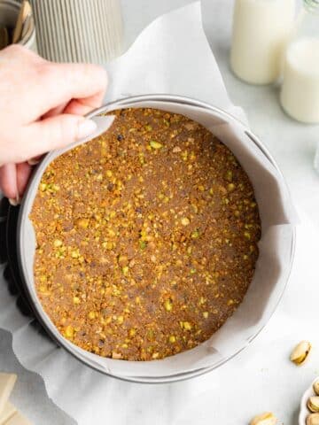 a no-bake pistachio cookie crust pressed into the base of a lined cheesecake pan.
