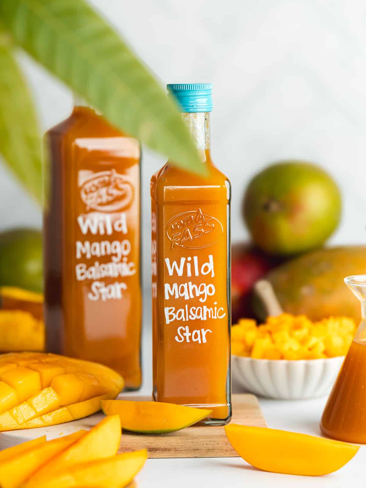 two bottles of wild mango balsamic vinegar with fresh mangoes scattered around.