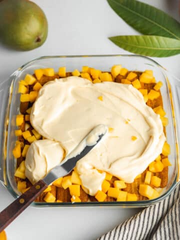 spreading mango mascarpone over a mango tiramisu with an offset spatula.