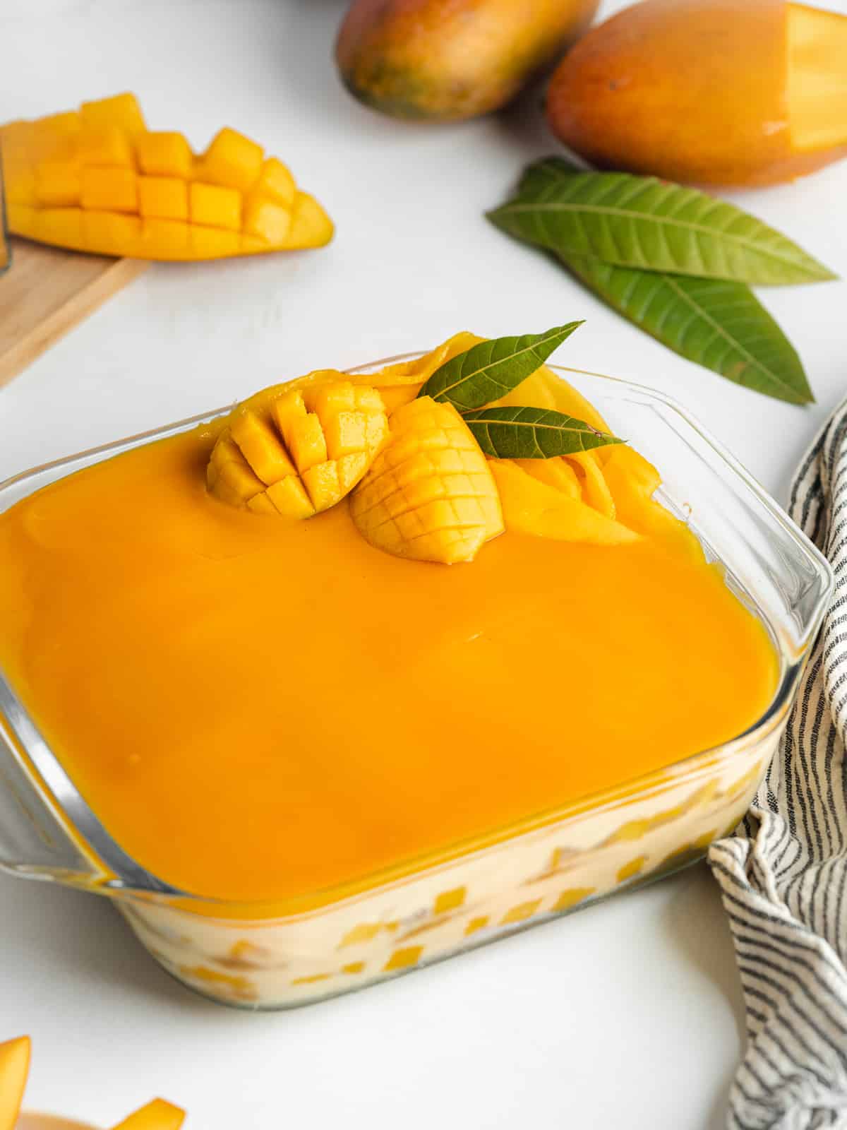 a mango tiramisu in a glass dish topped with fresh mango and mango leaves.