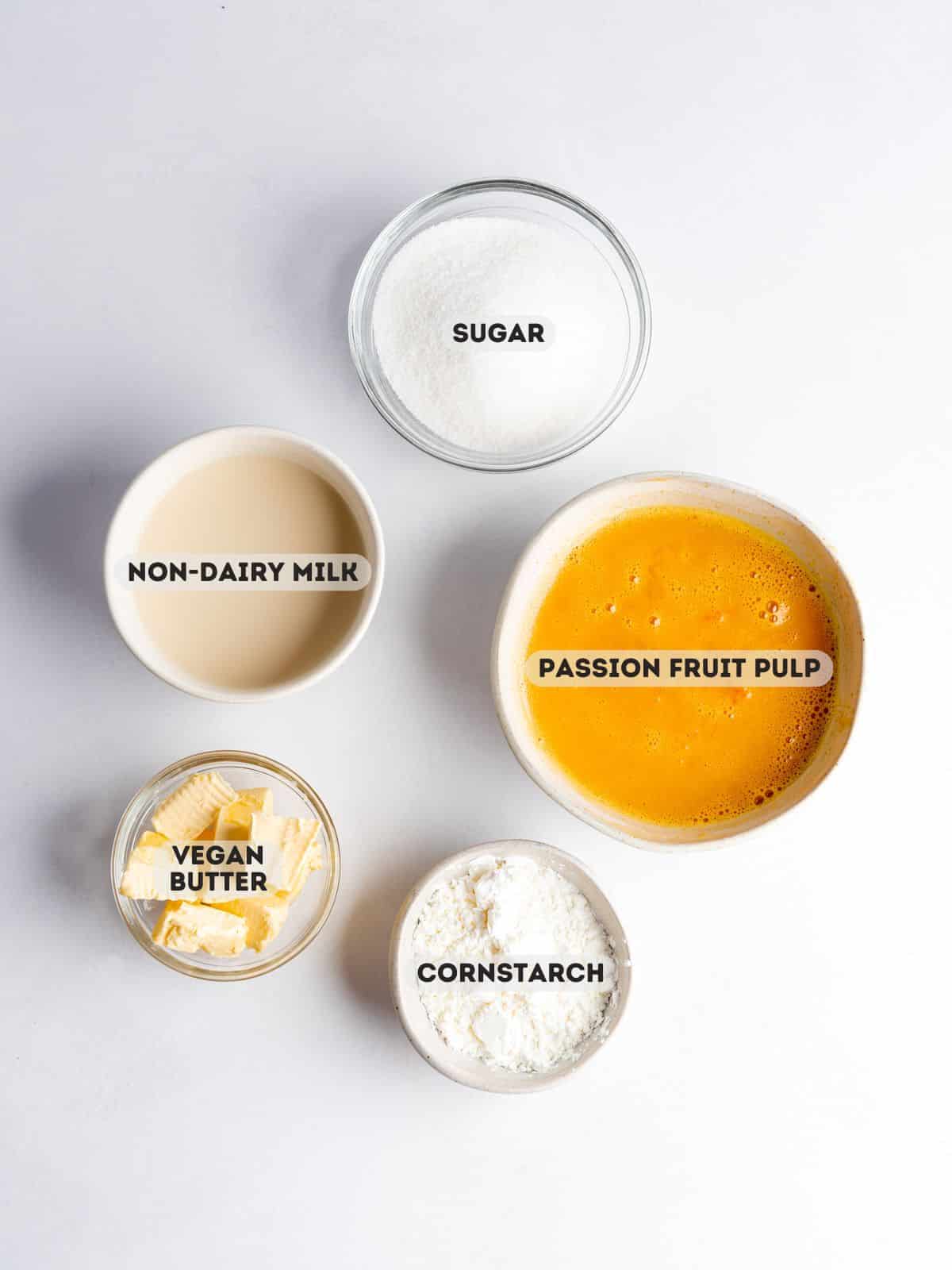 Ingredients for passion fruit curd measured out in bowls on a white surface.