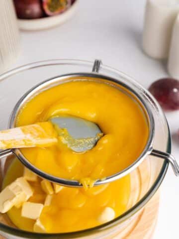 pressing passionfruit curd through a sieve into a bowl with cold butter cubes.