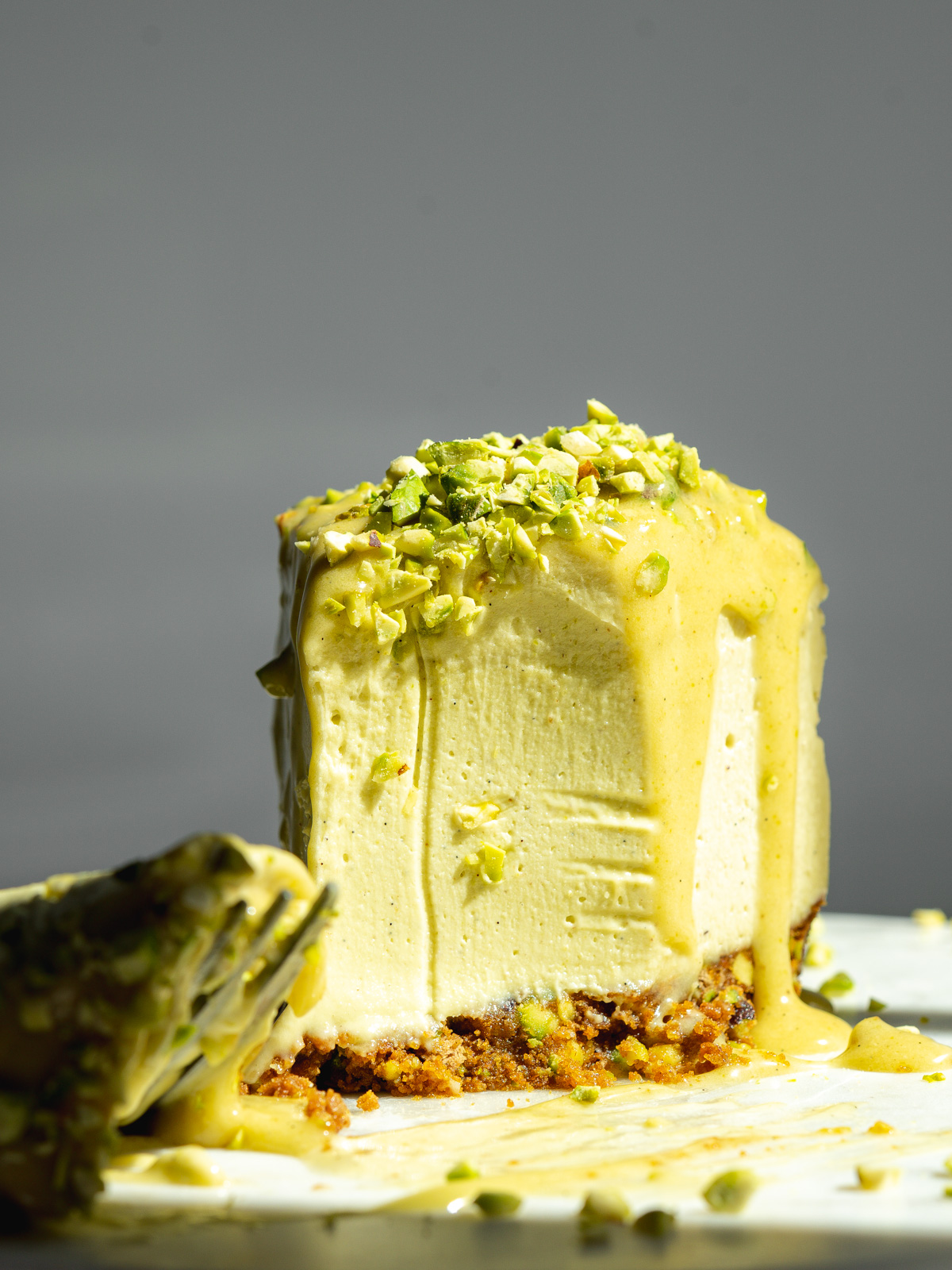 a slice of pistachio cheesecake with sunlight shining on it and a biteful taken away, showing the creamy consistency.