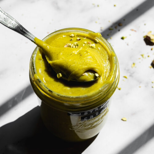 a mason jar filled to the top with pistachio crema with a spoonful sitting on top.