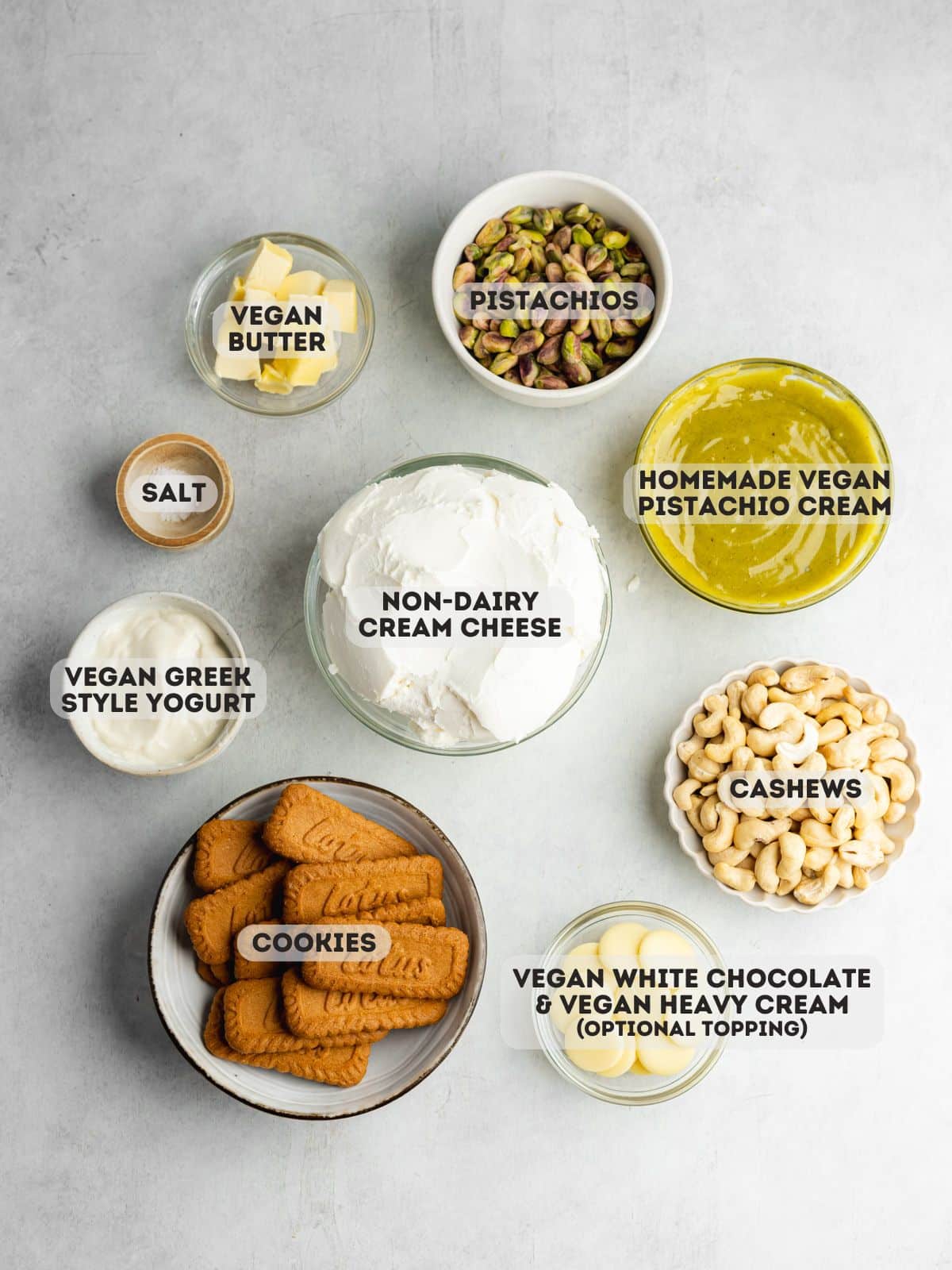 ingredients to make vegan pistachio cheesecake measured out in bowls on a gray surface.
