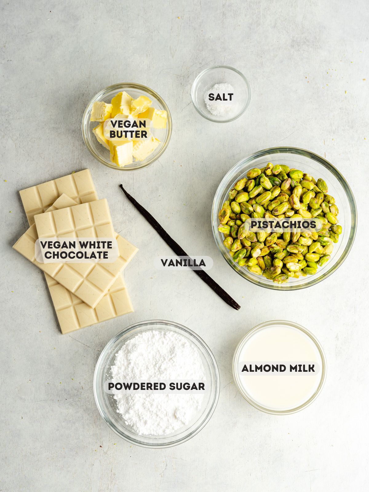 ingredients to make vegan pistachio cream measured out in small glass bowls on a gray table.