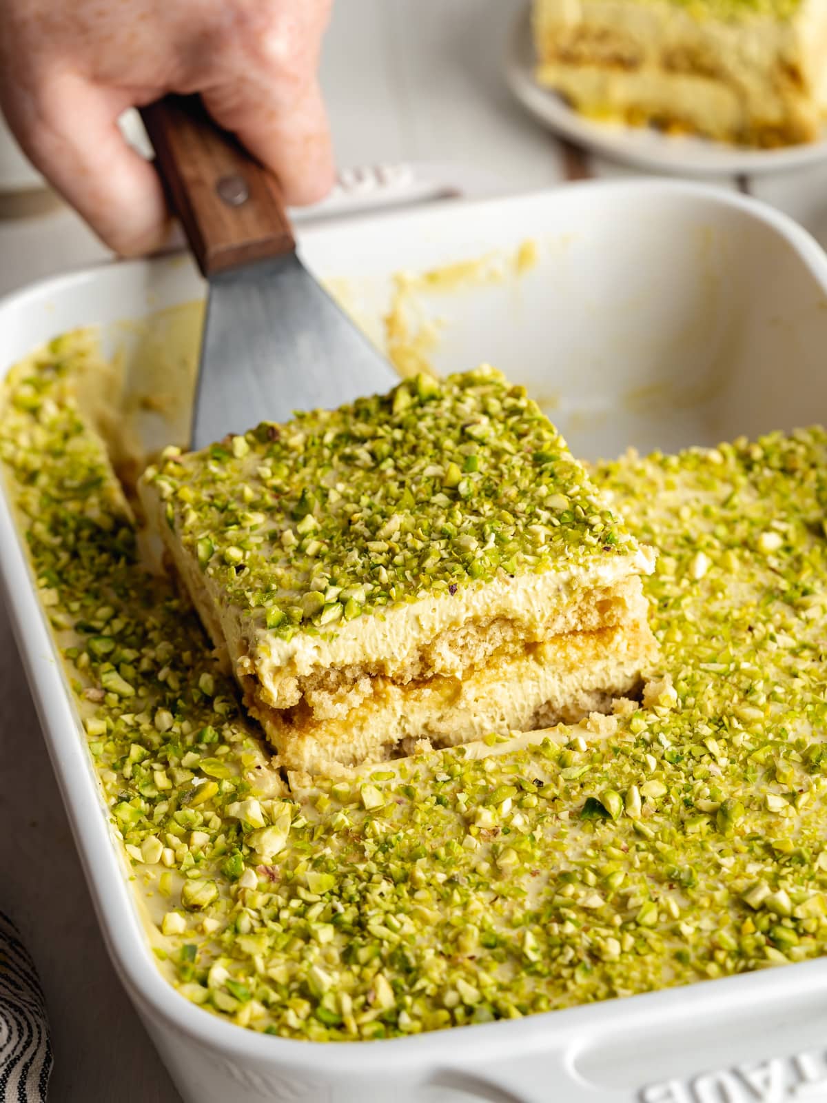 a slice of vegan pistachio tiramisu being lifted away from the dish.