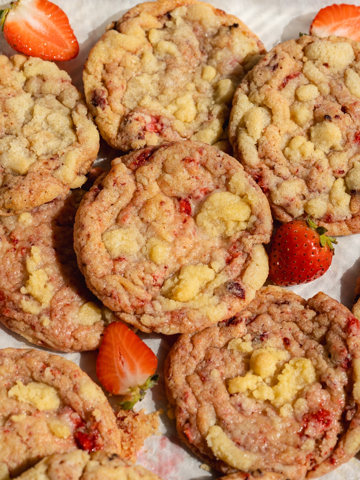 strawberry cookies with crumble topping and fresh strawberries scattered around on a baking sheet.