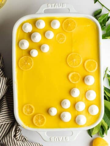 lemon curd tiramisu in a staub baking dish topped with piped vegan whipped cream and lemon slices.
