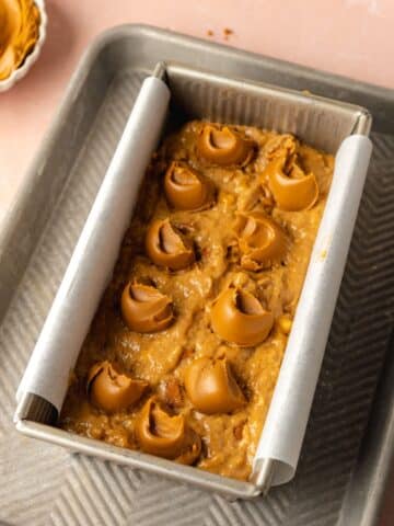 biscoff banana bread batter in a lined loaf tin with dollops of cookie butter scattered on top.