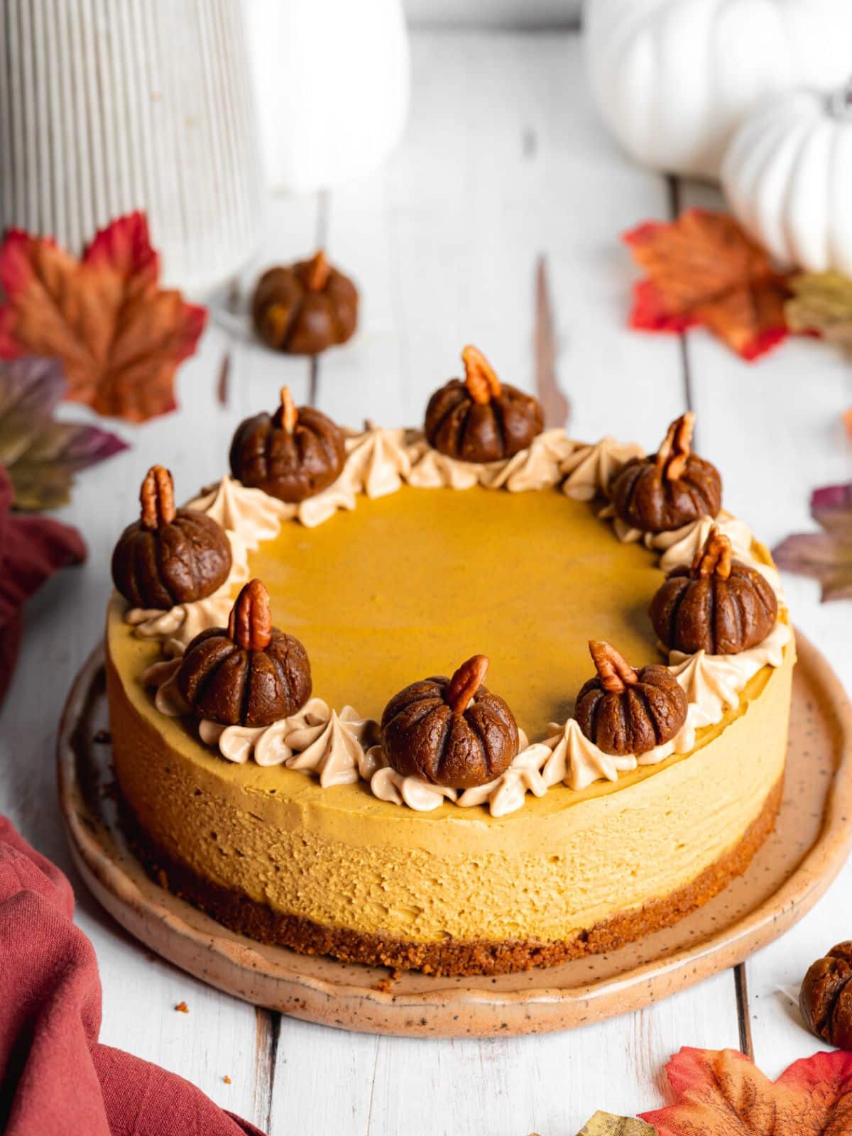 a pumpkin cheesecake on a brown ceramic plate topped with pumpkin truffles with autumn leaves scattered around the scene.