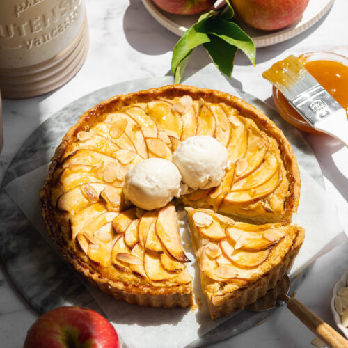 a vegan french apple tart with two scoops of ice cream and direct sunlight shining on it showing the bright colors.