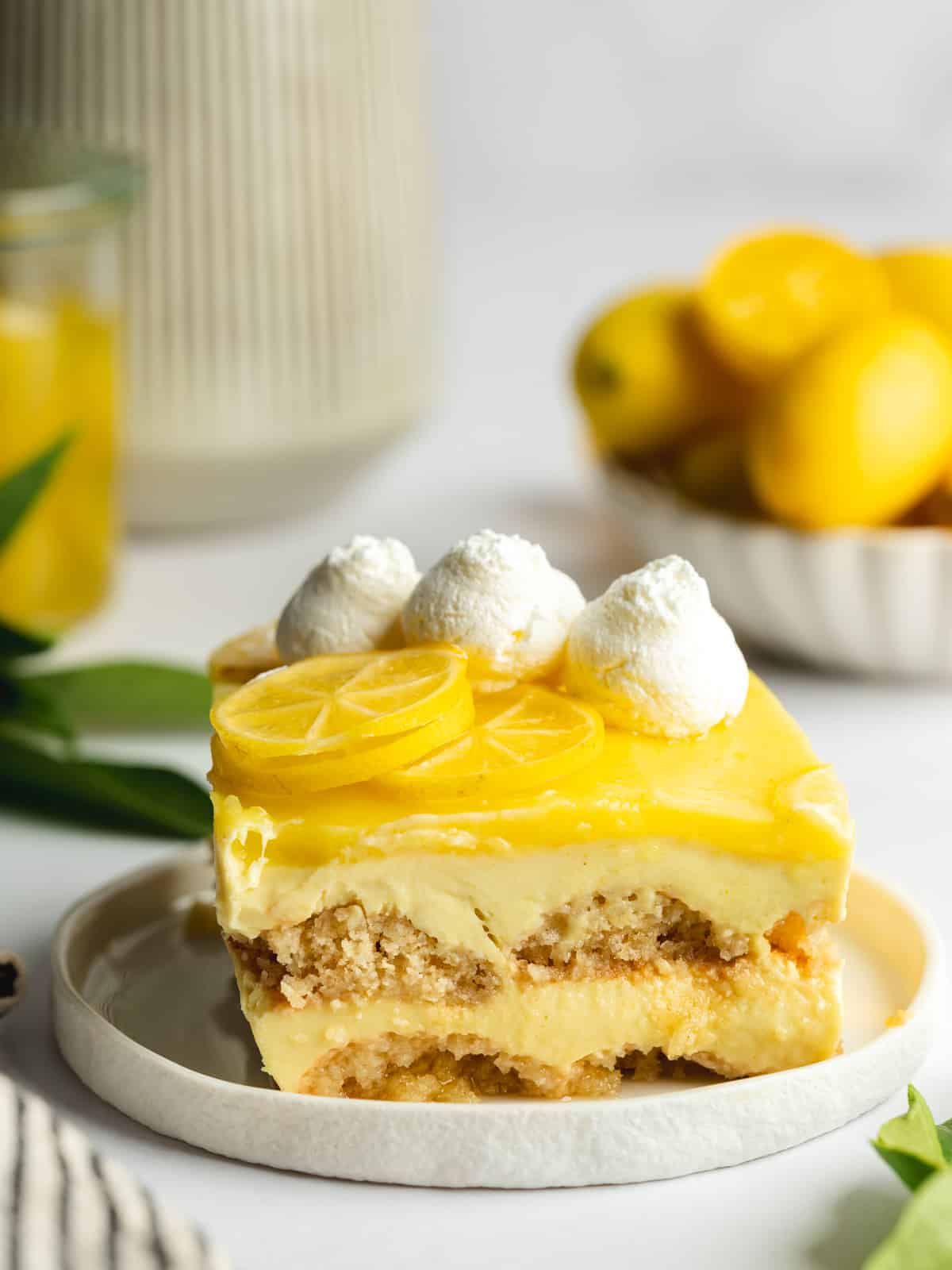 a slice of limoncello tiramisu topped with lemon curd, whipped cream, and lemon slices on a ceramic plate.