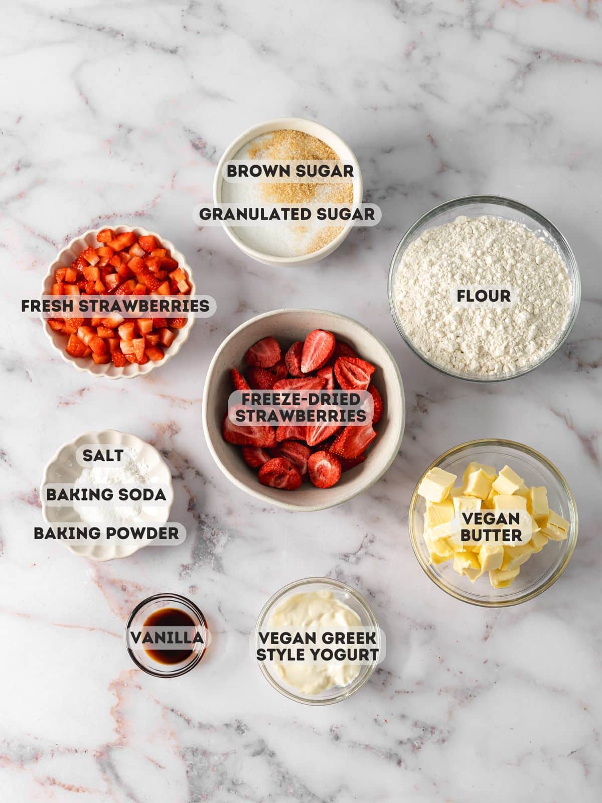 ingredients for strawberry shortcake cookies measured in bowls on a marble surface.