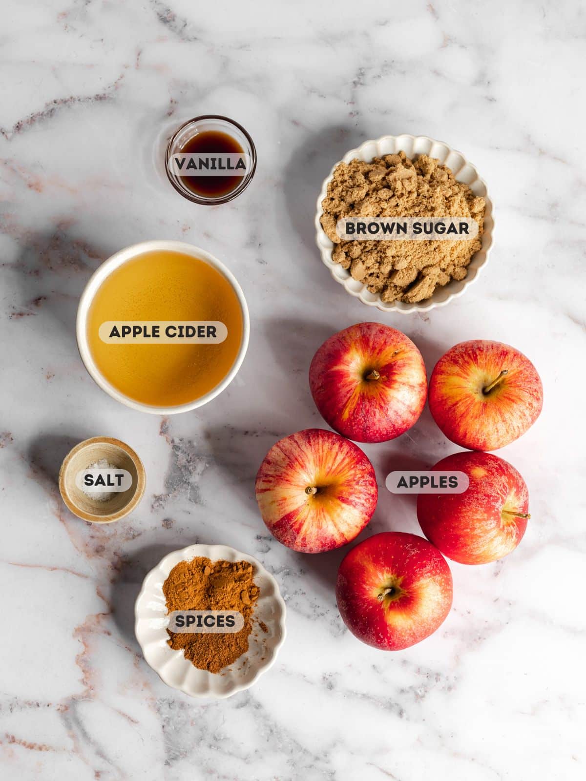 ingredients for apple butter measured out in bowls on a marble surface.