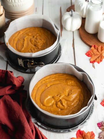 2 cake pans filled with pumpkin cake batter before baking.