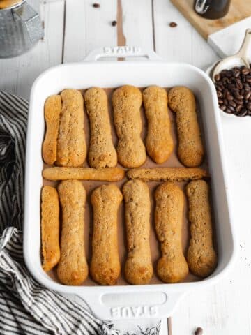 ladyfinger cookies arranged in a layer on top of chocolate mascarpone in a baking dish.