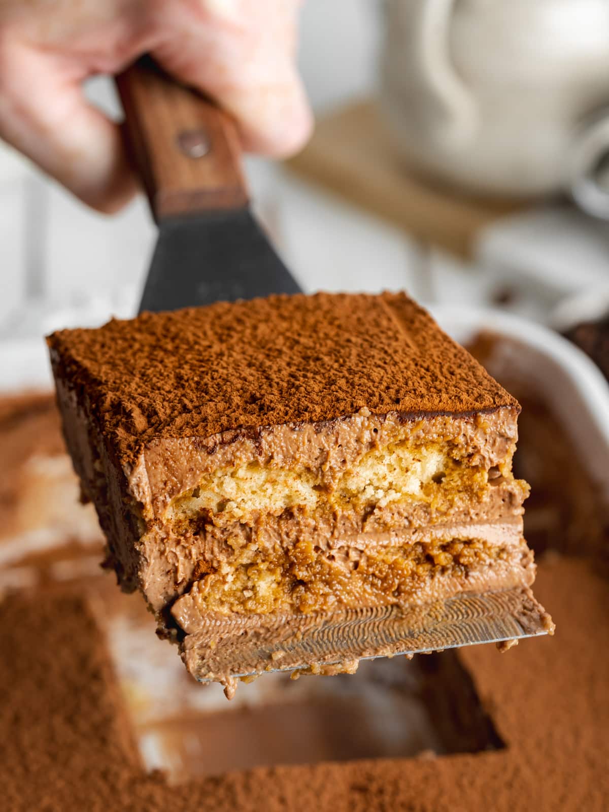 a slice of chocolate tiramisu being lifted out of a staub baking dish.