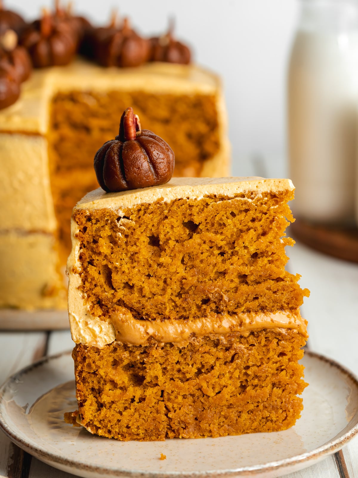 a slice of fluffy pumpkin cake with a mini biscoff pumpkin on top of a ceramic plate.