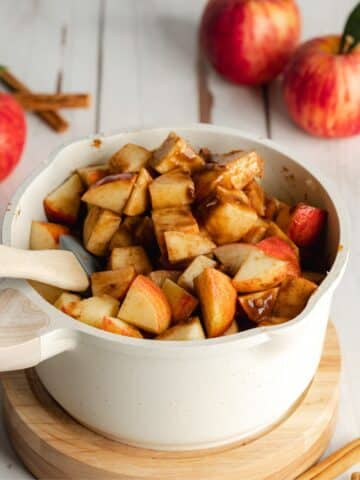 chopped apples with apple cider and spices in a white saucepan.