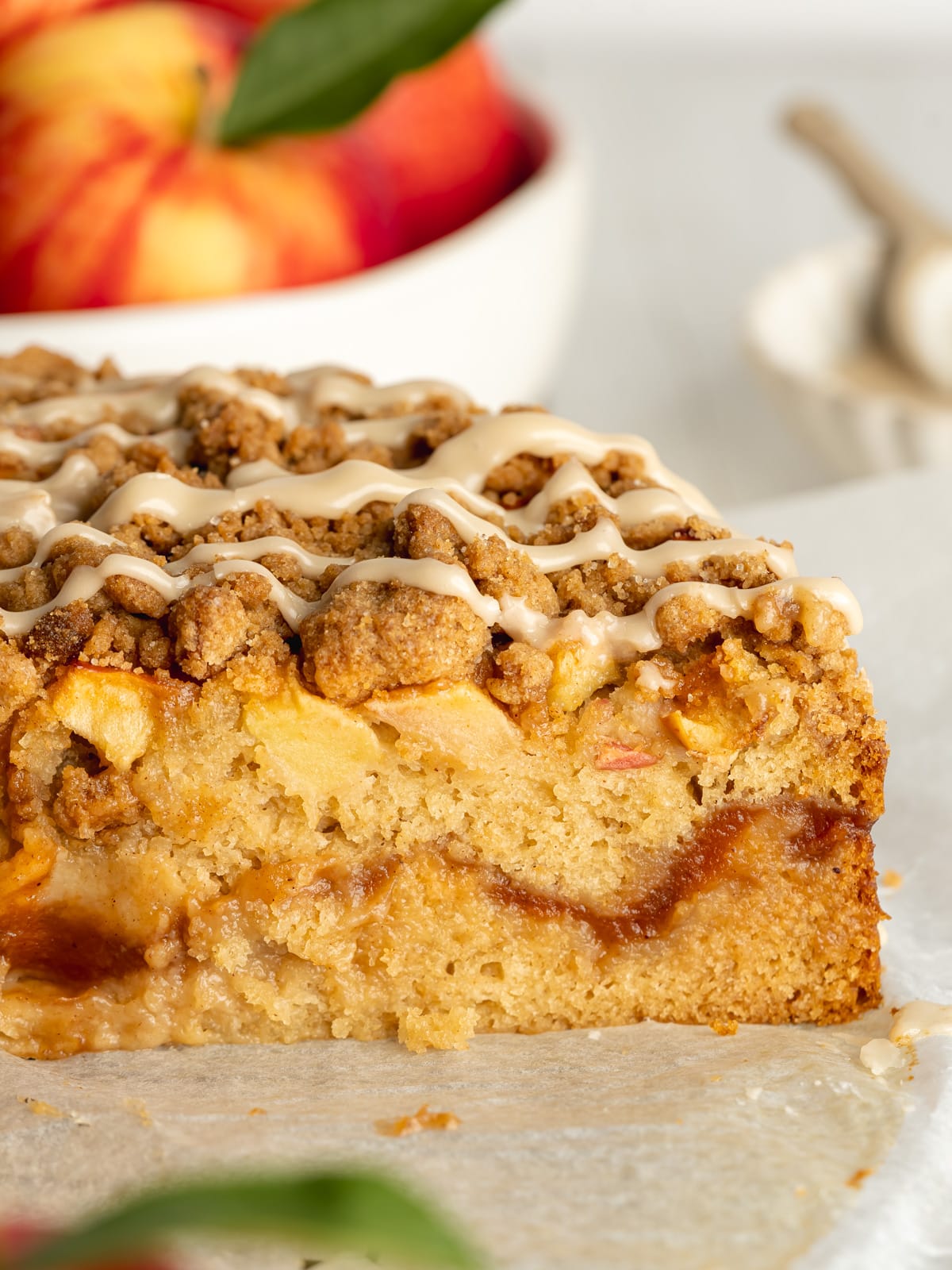 cross section of vegan apple coffee cake with apple butter filling and a bowl of fresh apples in the background.