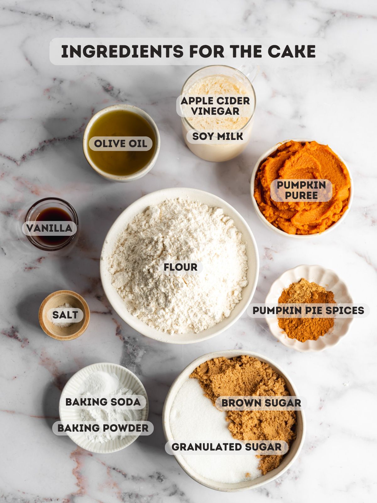 ingredients for vegan pumpkin cake measured in bowls on a marble surface.