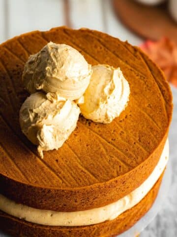 a pumpkin sandwich cake with three scoops of frosting on top before they're smoothed out with an offset spatula.