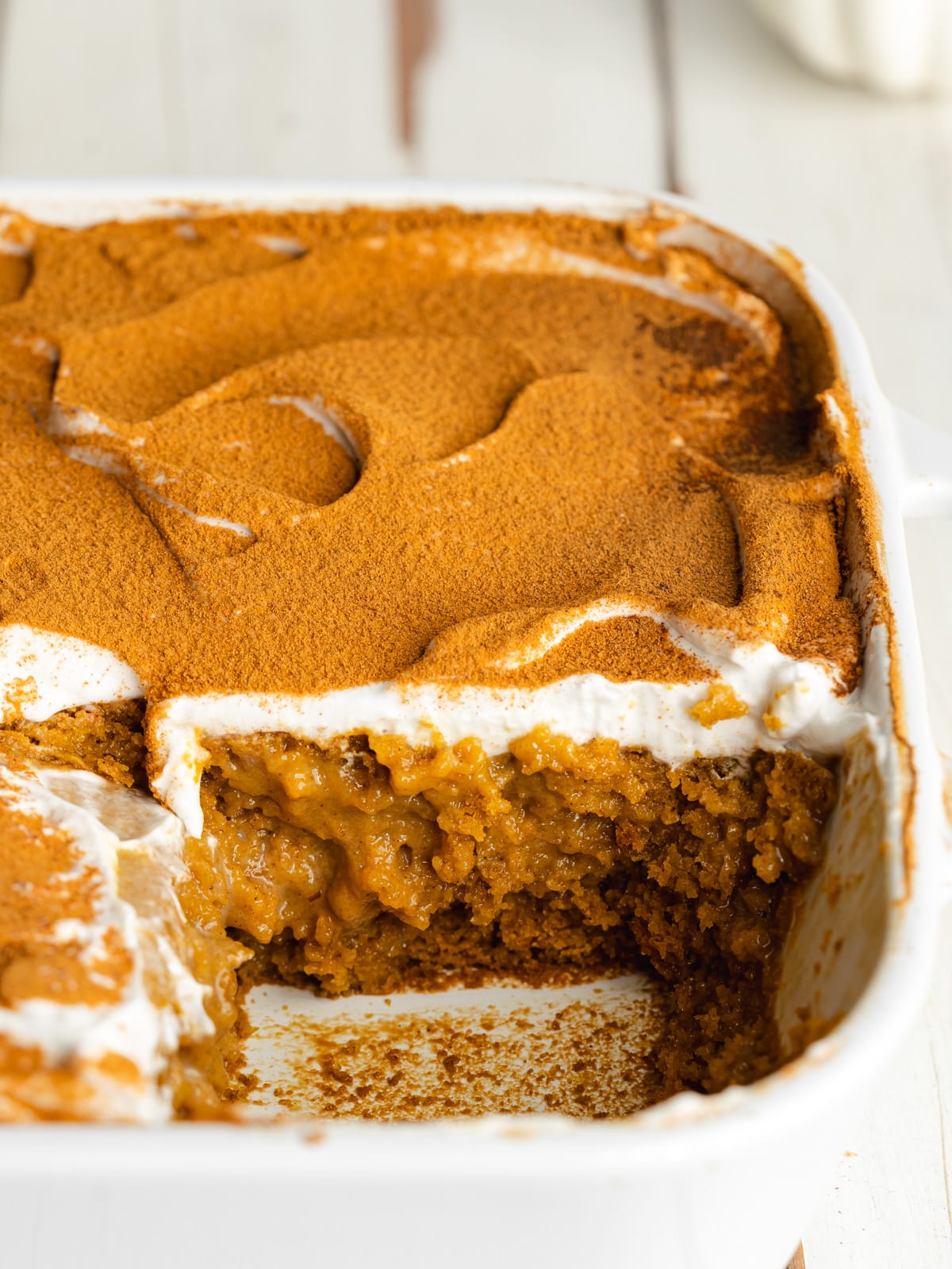 pumpkin tres leches in a white staub pan with a splice missing showing the moist texture.