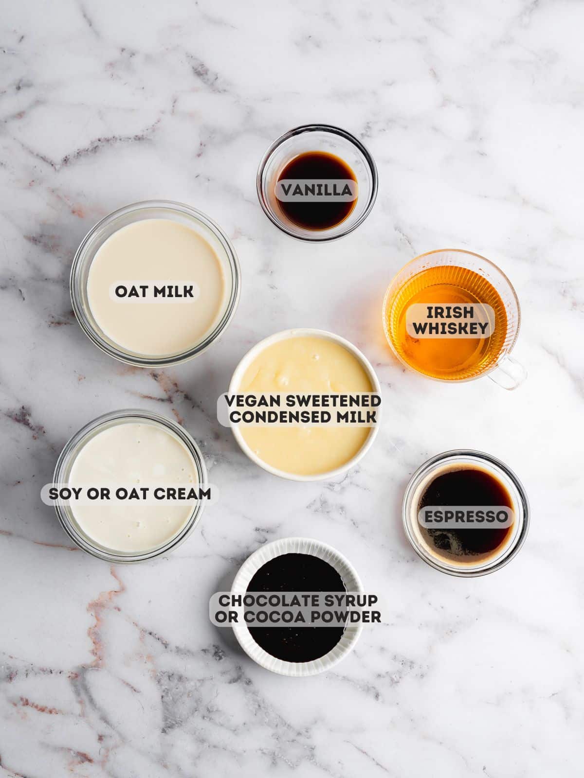 ingredients for homemade vegan baileys measured in bowls on a marble surface.