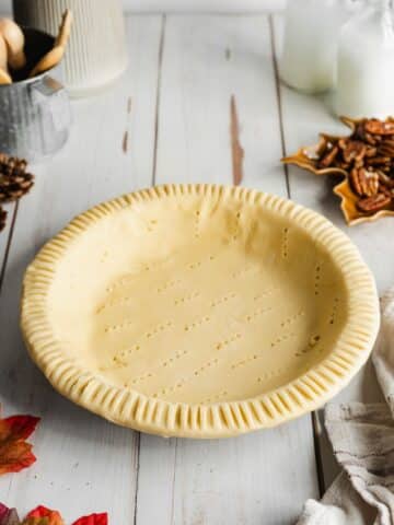 vegan pastry crust in a pie tin with holes pierced into it with a fork.